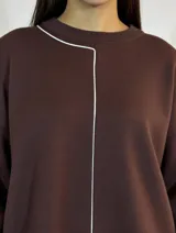 Buzo de punto color marrón con cuello redondo y detalle de costura vertical en contraste color blanco. Presenta mangas largas con puños acanalados y un corte relajado con aberturas laterales en el ruedo.