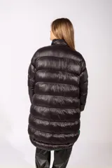 Campera puffer larga de color negro con acabado brillante, cierre frontal con botones a presión y cuello alto. Presenta un parche circular en la manga izquierda.