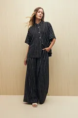 Conjunto de camisa y pantalón a rayas verticales en blanco y negro. La camisa es de manga corta, confeccionada en viscosa suave y fluida, con cuello clásico y botones al frente. El pantalón es de corte palazzo, con cintura alta y pernera ancha.