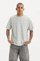 Remera de manga corta con cuello redondo y calce estándar. Presenta un estampado geométrico con líneas horizontales en tonos pasteles, azul y amarillo.