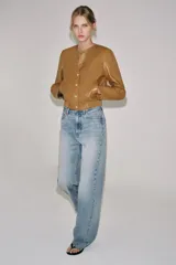Campera bomber de cuero 100% color tostado de la ZARA WOMAN COLLECTION, con cuello redondo, manga larga, bolsillos delanteros ribeteados y cierre frontal con botones metálicos en relieve. Presenta elástico fruncido en el dobladillo inferior.
