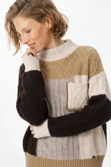 Sweater de punto con diseño patchwork en tonos tierra, crudo y marrón. Presenta cuello alto acanalado, mangas largas y un bolsillo frontal tipo parche con detalle de trenzas.