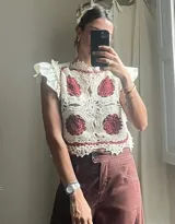 Top sin mangas de crochet color crudo con motivos florales circulares en color bordó. Presenta cuello alto y volados en los hombros.