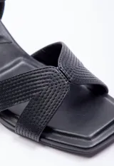 Sandalia alta de símil cuero negro con taco geométrico de 7.5 cm. Posee tiras cruzadas en el empeine con diseño pespuntado y tira ajustable con hebilla en el tobillo.