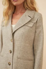 Tapado largo de corte recto confeccionado en lana fina sin teñir. Presenta cuello solapa, cierre frontal con botones, bolsillos laterales con tapa y detalles aplicados en la parte delantera. Incluye forro interior y tajo en la espalda.