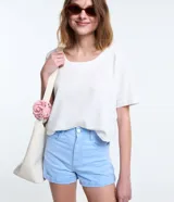 Short de sarga color blanco, de cintura alta, con bolsillos delanteros y traseros, trabillas para cinturón y bajo plegado. Cuenta con cierre frontal de botón y cremallera.