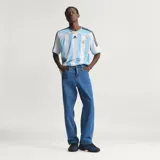 Pantalón de denim azul de corte holgado, tiro medio y diseño clásico con las tres tiras características de Adidas a lo largo de los laterales.