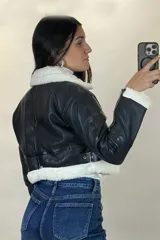 Campera tipo gamulán de cuero sintético negro, con interior y detalles de cuello y puños en corderito blanco. Presenta cierre frontal, cierres en los puños y correas ajustables en la cintura.