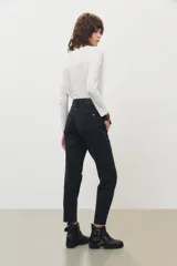 Jean de corte mom en color negro, con diseño de tiro alto, cinco bolsillos y detalle de rotura en la rodilla izquierda.