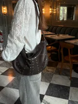 Bolso bandolera de cuero marrón oscuro con tachas doradas.