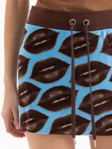 Minifalda de tiro medio y silueta entallada al cuerpo, con estampado de labios marrones sobre fondo celeste. Cuenta con cintura elástica marrón y cordón ajustable.