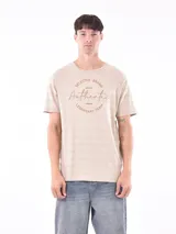 Remera de manga corta color beige con diseño de rayas horizontales sutiles en la textura de la tela y estampado circular en el pecho con la frase 'Selected Brand Authentic Legendary Team'.