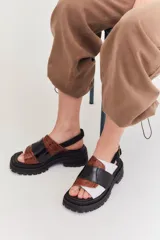 Sandalias de plataforma con suela track negra. Presentan un diseño de tiras anchas combinadas en cuero con textura de reptil color marrón y una franja central de charol negro. Incluyen una tira trasera elástica para mayor sujeción.