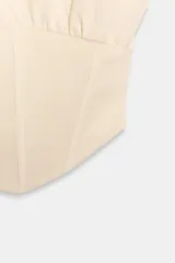 Top tipo corsetero color beige, confeccionado en algodón, con cuello redondo, manga sisa y bajo asimétrico con rib.