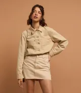 Campera color beige confeccionada en sarga de algodón, de corte regular, con cuello camisero, cierre abotonado, manga larga, bolsillos frontales y recortes.