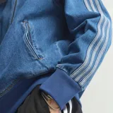 Campera adidas Adicolor Firebird de denim azul, con cierre frontal, bolsillos laterales, cuello alto y las icónicas tres tiras de la marca en las mangas.