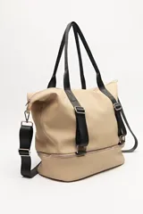 Bolso tipo tote color beige con detalles en negro, confeccionado en material sintético liso. Cuenta con doble asa superior, correa ajustable y extraíble, cierre principal superior y un compartimento inferior independiente con cierre. Presenta correas decorativas verticales con hebillas metálicas y logo grabado en la base.