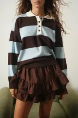 Sweater tipo chomba de tejido bremer con diseño de rayas horizontales en color marrón y celeste. Presenta cuello polo en color crema con cierre frontal de botones y mangas largas.