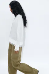 Jersey de cuello redondo y manga larga, color blanco, con bajo acabado en encaje combinado a tono.