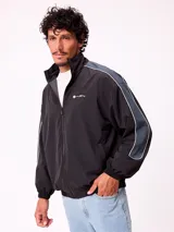 Rompevientos Rusty de nylon con cierre frontal, cuello alto y mangas largas con puños elásticos. Presenta paneles laterales en las mangas en tono gris oscuro con detalles de líneas blancas.