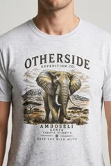 Remera blanca de manga corta con cuello redondo y estampa frontal de elefante con diseño de safari y texto.