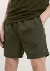 Bermuda deportiva de corte recto y diseño minimalista en color verde militar. Cuenta con cintura elástica, bolsillos laterales y un pequeño logo reflectante en la parte inferior de la pierna.