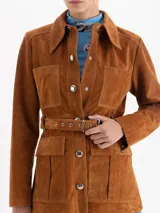 Parka de gamuza color ocre con diseño de estilo safari, cuello camisero, cierre frontal con broches metálicos, múltiples bolsillos frontales y cinturón ajustable con hebilla metálica.