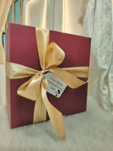 Caja de regalo artesanal color bordó con moño dorado, diseñada como experiencia de lujo para presentar un conjunto de lencería. Incluye elementos de regalo adicionales como perfume, rosa natural y dulces.