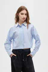 Camisa de algodón a rayas verticales en tonos celestes y blancos, con cuello camisero en contraste color blanco, manga larga y corte cropped.