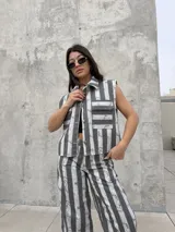 Chaleco de denim sin mangas, con cuello mao y cierre frontal con botones. Presenta bolsillos ojal en el pecho con solapa y un diseño a rayas verticales en tonos rosados y blancos con efecto desteñido.