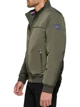 Campera bomber verde militar de poliéster, con cuello mao, cierre frontal con cremallera, dos bolsillos laterales con cremallera, puños y ruedo elásticos. Logo de Tommy Hilfiger bordado en el pecho.