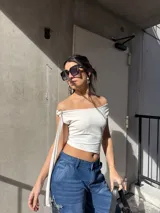 Top de jersey lycra color blanco, con escote off-shoulder asimétrico y tira larga ajustable con hebilla metálica en el hombro.