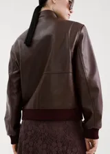 Chaqueta estilo bomber de cuero sintético marrón oscuro, con cierre frontal de cremallera, cuello alto abotonado y bolsillos frontales con solapa.
