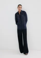 Camisa azul marino de lyocell y poliéster, con cuello camisero, manga larga, cierre frontal oculto con tapeta y detalles de apliques de strass y cristal en la parte delantera y las mangas.
