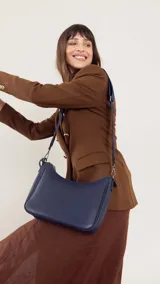 Bandolera de cuero sintético color marrón, con cierre trasero y división interna. Incluye correa de galón ajustable y un pequeño charm colgante.