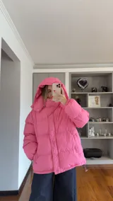 Campera puffer de corte holgado en color beige, con diseño acolchado, cuello alto y capucha desmontable. Cuenta con cierre frontal y botones a presión, además de puños elásticos.
