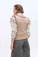 Chaleco tejido de punto color amarillo, con diseño calado, escote redondo y volados en los hombros y cuello. Cuenta con cierre frontal de botones forrados al tono.