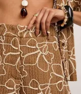 Short color marrón con estampado abstracto en blanco, texturizado, con trabillas en la cintura y cierre tradicional.