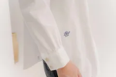 Camisa de manga larga color rosa claro con textura, cuello y puños blancos contrastantes. Los puños tienen tres botones rosados.