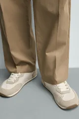 Zapatilla deportiva estilo barefoot, color marrón, con diseño de paneles en combinación de materiales y detalles en serraje. Cuenta con puntera redondeada y ancha, cordones en color crema y suela fina de goma flexible en contraste.