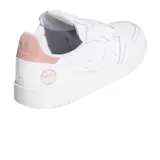 Championes Adidas modelo Supercourt W, de diseño clásico y minimalista en color blanco con detalles en rosa pastel en el talón. Presenta una estructura de cuero con costuras acolchadas y perforaciones laterales, sobre una suela de goma resistente.