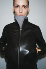 Cazadora tipo bomber de piel 100%, color marrón oscuro, con cuello subido y cierre frontal con cremallera metálica. Cuenta con bolsillos delanteros, forro interior y puños y bajo elásticos acanalados.