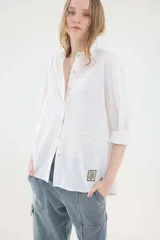 Camisa de lino blanca, de silueta oversize y calce relajado, con mangas largas y detalles de puntillas en la delantera.