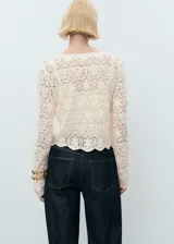 Cardigan de punto con diseño de crochet color crudo, cuello redondo, manga larga, cierre frontal con botones y bajo festoneado.