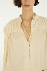 Blusa de mangas largas con puños abotonados, cuello alto con detalles de encaje y cierre frontal de botones forrados, confeccionada en tejido liviano con aplicaciones caladas.