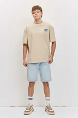 Remera de corte oversize color blanco tiza, de manga corta y cuello redondo, con pequeño estampado gráfico azul en el pecho.
