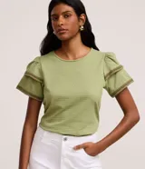 Blusa verde de cuello redondo y manga corta abullonada de doble volante, con bordes decorados en tejido efecto ganchillo en contraste.