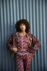 Campera impermeable con capucha y cierre frontal, con estampado de hojas en tonos marrones y ocres. Tiene bolsillos laterales ocultos y cordón ajustable en la cintura.