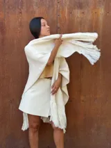 Ruana tejida de lana en color crudo, con diseño de flecos en los bordes. Es una prenda versátil y abrigada, ideal para complementar diversos looks.