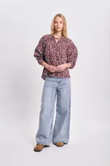 Blusa de estilo boho color bordó con estampado floral blanco, cuello redondo con cordones ajustables y mangas largas abullonadas con puños elásticos.